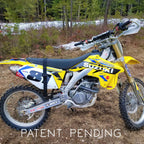 Suzuki dirt bike in a forested area with 'Patent Pending' text.